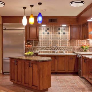 A modern kitchen featuring wood cabinets, an island, and colorful pendant lighting.
