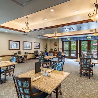 A spacious and elegantly decorated dining area with neatly arranged tables and chairs, featuring soft lighting and large windows.