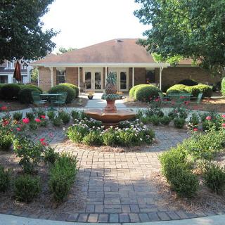 A beautifully landscaped garden with a central fountain surrounded by flowers and bushes.