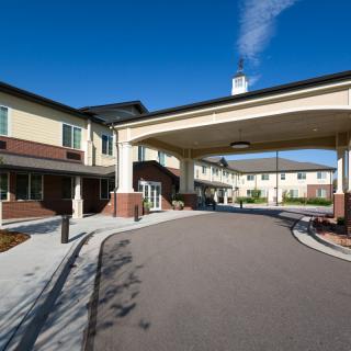 The image shows the entrance and driveway of a modern building on a clear day.