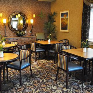 A cozy dining area with elegantly arranged tables and chairs, featuring a decorative mirror and green plants for ambiance.