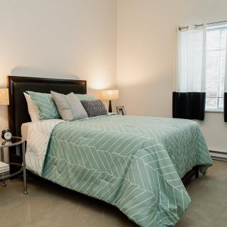 A cozy bedroom with a neatly made bed, featuring a green comforter and several pillows. The room is softly lit by lamps on either side of the bed.