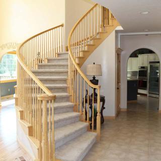 A bright, spacious home interior featuring a curved wooden staircase with carpeted steps.