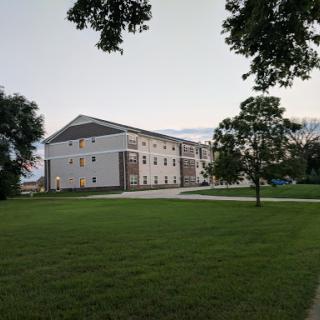 A modern building set against a serene evening sky, surrounded by lush green grass and trees.