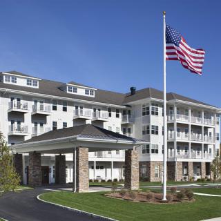 A four-story residential building with a covered entrance and a large American flag in front.
