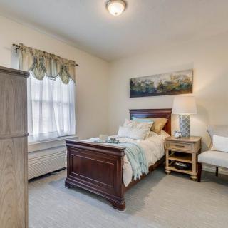 A cozy bedroom featuring a single bed, nightstand with a lamp, and a window adorned with curtains.