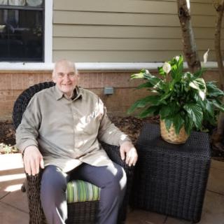 A man seated outdoors on a patio next to a potted plant.