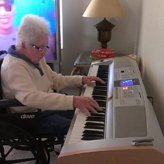 An elderly person in a wheelchair playing music on a keyboard at home.