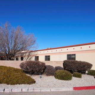 A single-story building surrounded by desert shrubbery under a clear blue sky.