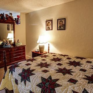 A cozy bedroom with a quilted bedspread, wooden dresser, and warm lighting.