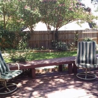 A sunny backyard patio with striped chairs and lush greenery.