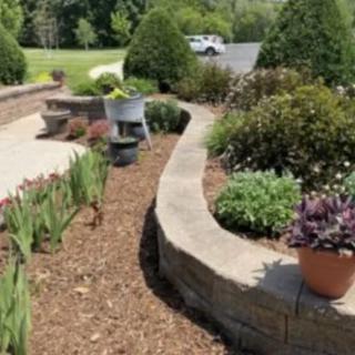 A beautifully landscaped garden with a stone walkway, potted plants, and outdoor seating on a sunny day.