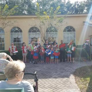 A group of people gathered outside in front of a building with arched windows on a sunny day.