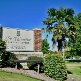 Entrance sign for The Palmetto library surrounded by greenery and a palm tree.