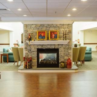 A cozy living room interior featuring a stone fireplace with framed art, surrounded by comfortable seating and warm lighting.
