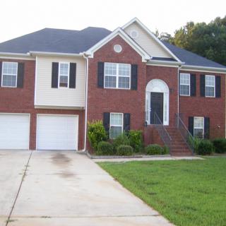 A two-story suburban house with a brick exterior, driveway, and a green lawn.