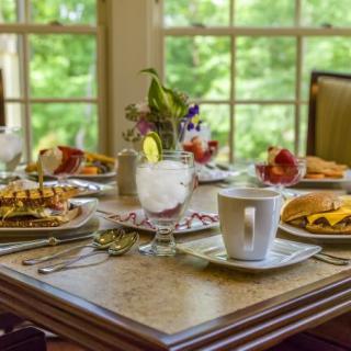 A beautifully set breakfast table with a variety of dishes and drinks, overlooking a scenic window view.