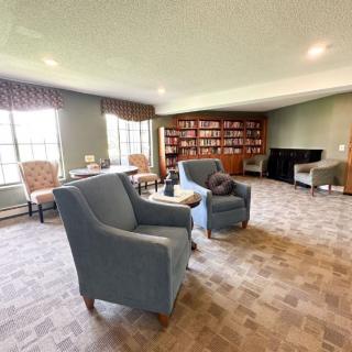 A cozy living room featuring armchairs, bookshelves, and large windows.