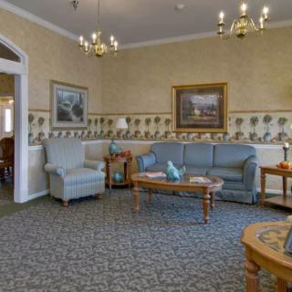 A traditionally decorated living room with sofas, armchairs, and a coffee table, featuring artwork and chandeliers.