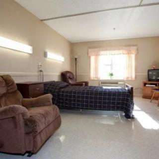 A hospital room with a bed, recliner chair, television, and a window allowing natural light.