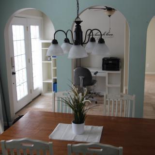 A cozy dining room with a wooden table, white chairs, and a hanging chandelier.