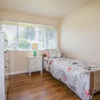 A minimalistic bedroom with a single bed, floral bedding, and a small bedside table by the window.