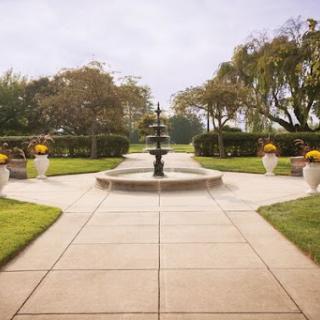 A serene garden pathway featuring a central fountain surrounded by lush greenery and decorative planters.