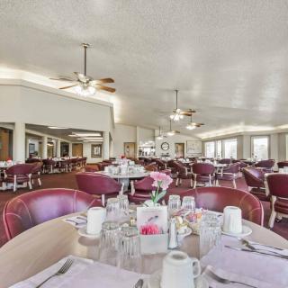 A spacious dining hall with neatly arranged tables and chairs, featuring bright lighting and ceiling fans.