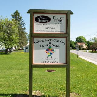 A wooden sign for a child care and learning center displayed outdoors by the roadside.