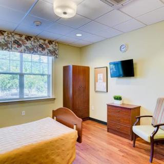A cozy and well-lit bedroom with a bed, chair, wardrobe, and wall-mounted TV.