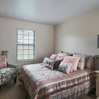A cozy and stylish bedroom featuring a comfortable bed adorned with various pillows and a charming armchair.