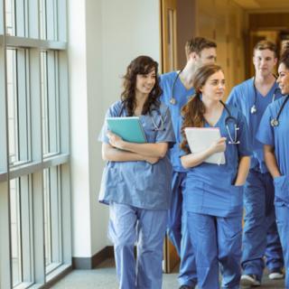 A group of medical students walking in a hospital corridor, wearing scrubs and carrying notebooks.