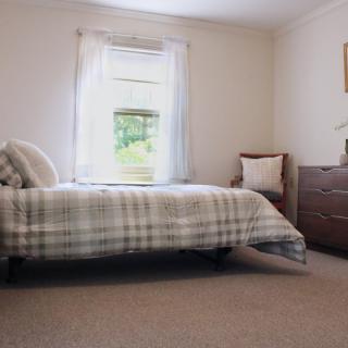 A minimalist bedroom with a plaid bedspread and a wooden dresser next to a window.