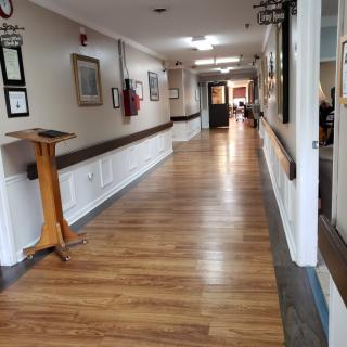 A long hallway with wooden floors in a healthcare facility, adorned with paintings on the walls.