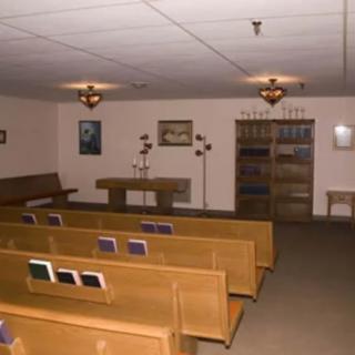 An indoor chapel with wooden benches and an altar, featuring religious decor and books.