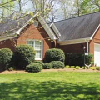 A suburban brick house with a well-maintained lawn and surrounding greenery.