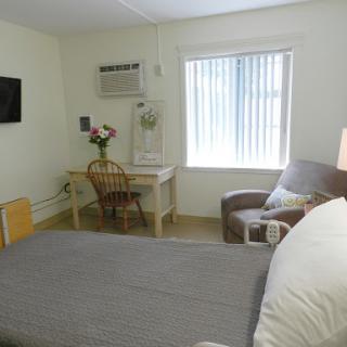 A cozy hotel room featuring a bed, desk, and comfortable seating with natural light coming through the window.