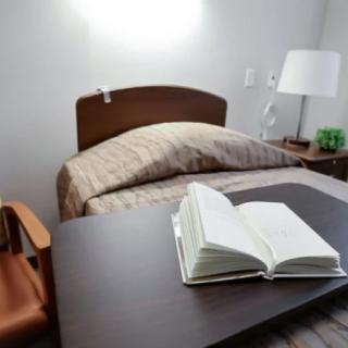 A cozy bedroom setup with an open book on a desk beside the bed.