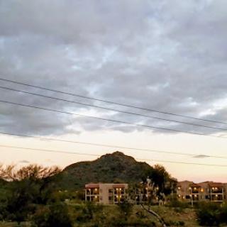 A serene view of a mountain under a cloudy sky, with buildings in the foreground.