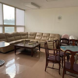 A spacious living room featuring a comfortable sofa, wooden dining chairs, and tables, with plenty of natural light coming in from the windows.