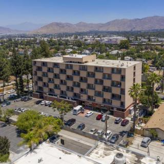 Aerial view of a multi-story building with a parking lot, surrounded by trees and mountains in the background.