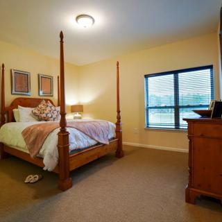 A cozy bedroom with a four-poster bed, bedside lamp, and a window allowing natural light.