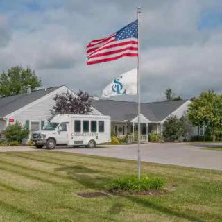 A building with a parked bus and an American flag flying in the foreground on a cloudy day.