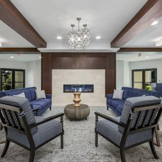 A modern living room featuring blue sofas around a central fireplace, with elegant wood beams and a chandelier overhead.