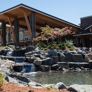 A modern building with a sloped roof is surrounded by a landscaped garden featuring a waterfall and pond.