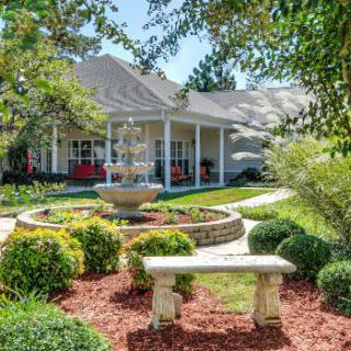 A beautiful garden with a fountain and bench in front of a house.