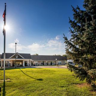 A sunny day with a building and flagpole in the background, surrounded by a lush green lawn and trees.