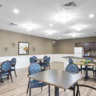 A spacious dining area with multiple tables and chairs, adjacent to a kitchenette.