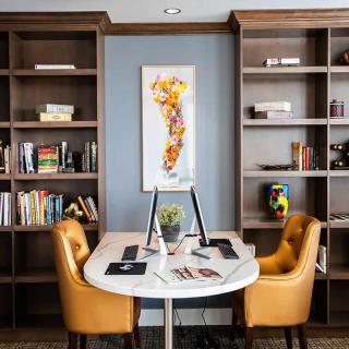 A modern office setting featuring a round desk with two chairs, surrounded by bookshelves and colorful artwork.