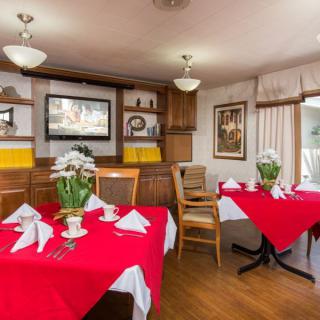 A cozy restaurant dining area with tables set in red tablecloths and white napkins, featuring wooden furniture and decorative elements.